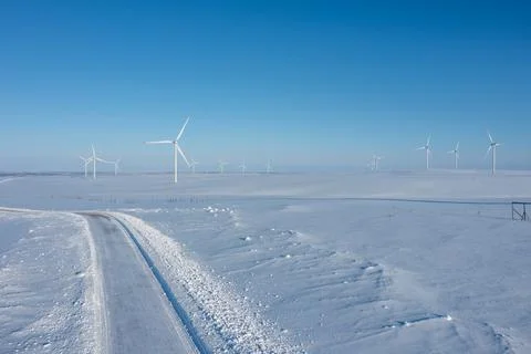 High-angle drone view of a clear snowy road leading towards a distant wind farm Stock Photos