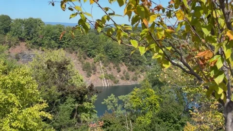 High-angle drone view looking across a calm blue quarry toward steep rocky Stock Footage 346657574