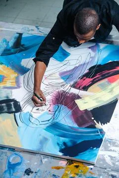 High angle image of a black man drawing lines on a big canvas with a painting Stock Photos
