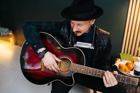 High angle image of middle aged man in a hat sitting on a stool, plaing guita Stock Photos
