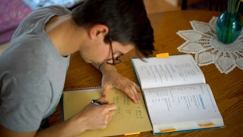 High angle looking down at a teenage boys paper and book as he works out math Stock Footage 89163766
