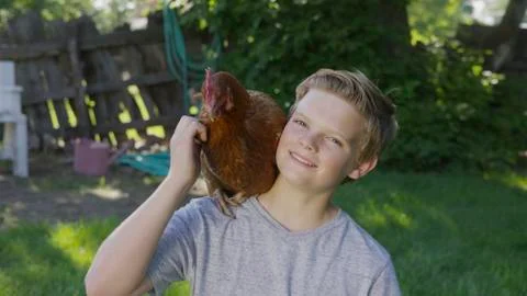 High angle portrait of smiling boy petting rooster on shoulder in backyard Stock Photos