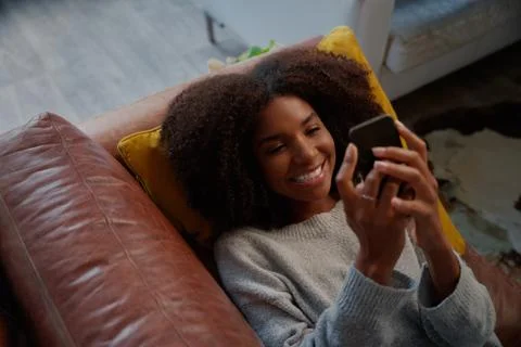 High angle portrait view of cheerful african woman lying on couch using Stock Photos