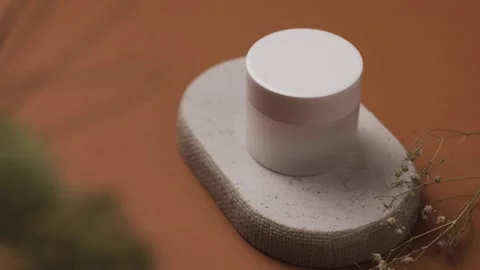 High angle reveal of white cosmetic cream jar on stone podium pull back shot Vídeos de archivo 342377399