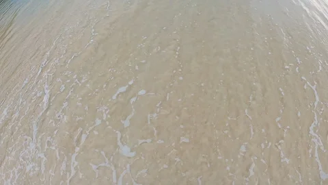 High angle shoreline view with pale blue water washing over smooth beige sand Stock Footage 338446142