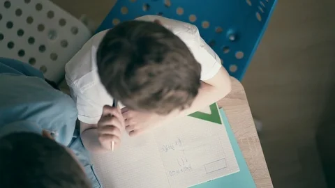 High-angle shot: Children perform school homework, sitting at a table, in a Stock Footage 105101100