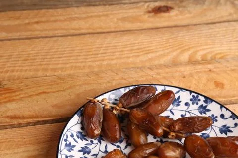 A high angle shot of dates on a china plate with floral patterns on a wooden  Stock Photos