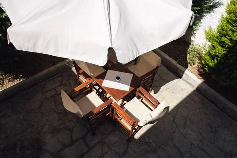 High angle shot of empty wooden table and chairs under white sun umbrella o.. Stock Photos