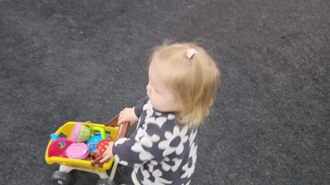 High-angle shot of little Sofia playing with a toy shopping cart Видео 335003534