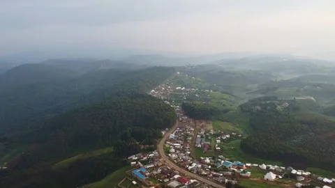 High angle shot reveals a town nestled amidst rolling hills and dense forest Stock Footage 317837372