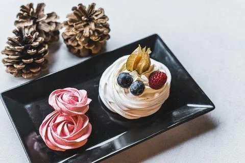 High angle shot of small meringue dessert with berries on black plate standing Stock Photos