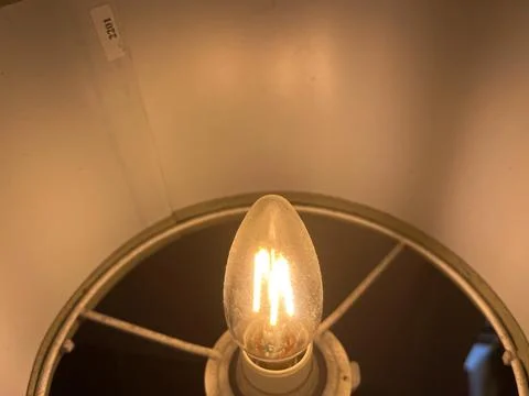 High-angle shot of a warm LED filament candle bulb glowing inside a lampshade Stock Photos