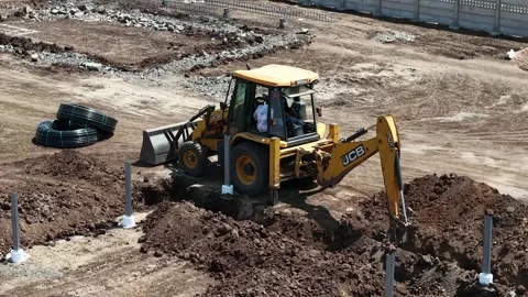 High angle shot of a yellow JCB backhoe loader digging a deep trench in dark Stock Footage 339912378