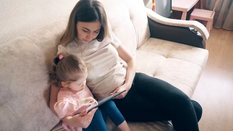 High-angle side shot: Young mother and sweet daughter are sitting on couch and Stock Footage 105115382