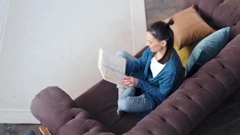High angle smiling casual young woman enthusiastically reading book turning page Vídeos de archivo 104223195