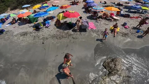 High angle of two men walking on crowded beach with camera pole Видео 280884468