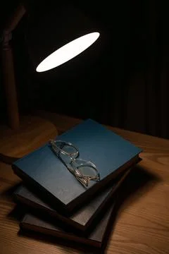 High angle vertical view of glasses and books under lamp in dim lit room. Stock Photos