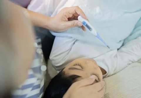 High angle view of Asian sick boy lying in bed with a thermometer in his mo.. Foto stock
