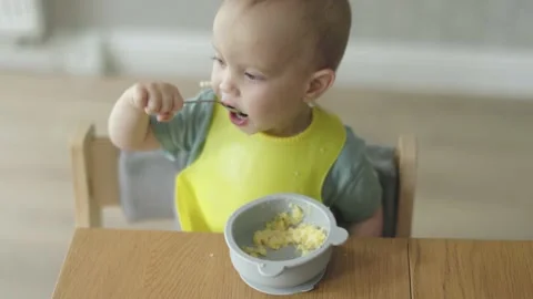 High angle view baby sitting at table learning to use spoon with food, eating Video stock 203944765