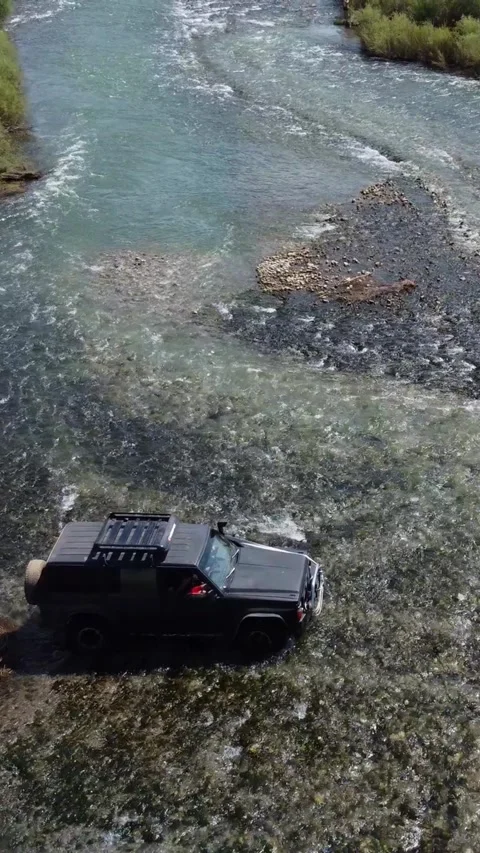 High angle view of black 4x4 off-road vehicle crossing wide mountain river Stock Footage 336690735