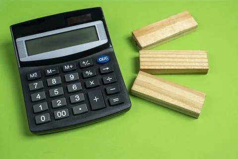 High angle view of a black calculator and three wooden blocks on a solid gr.. Stock Photos