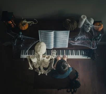 High angle view of boy playing piano while sitting by skeleton during Halloween Stock Photos
