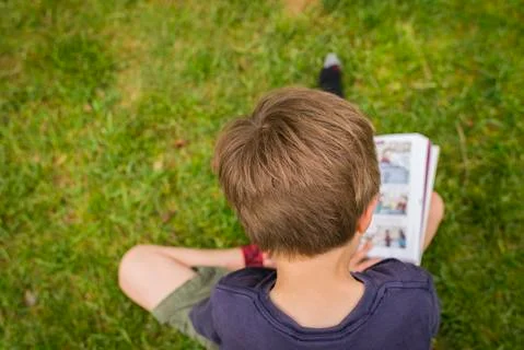 High angle view of boy reading comic book while sitting on grassy field at park Stock Photos