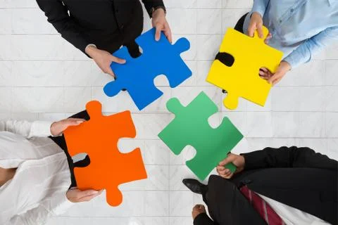 High Angle View Of Businesspeople Team Holding Colorful Puzzle Pieces In Hand Stock Photos