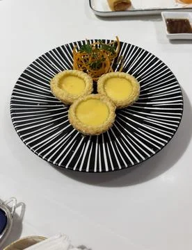 High angle view of Chinese dim sum egg tarts served on a black and white plate  Stock Photos