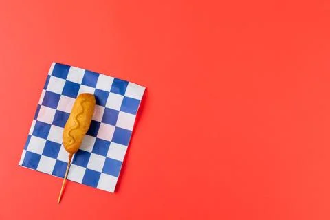 High angle view of corn dog with mustard sauce on checked pattern paper over red Stock Photos