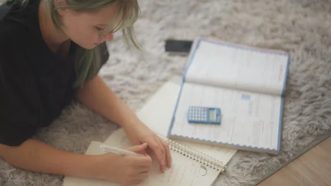 High angle view of diligent teenage girl lying on cozy carpet, solving math.. Video stock 318366822