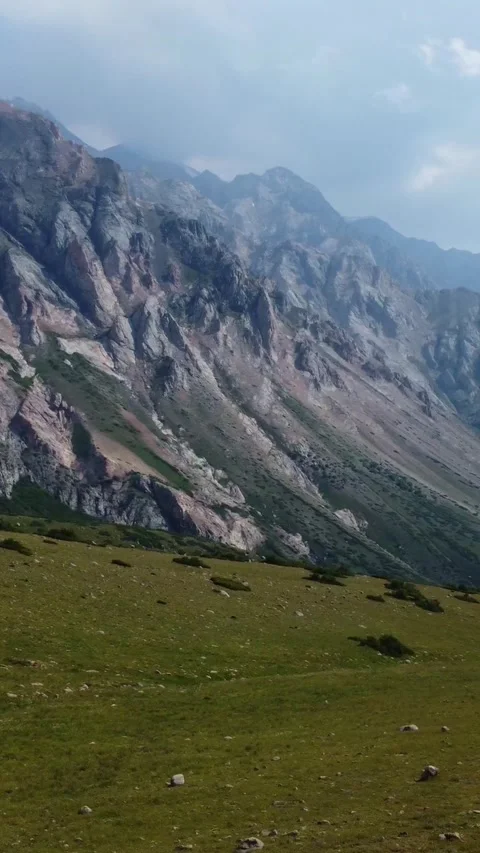 High angle view of an empty green alpine meadow below majestic steep cliffs Stock Footage 336693284