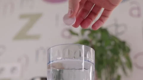 High angle view of hand dropping red vitamin tablet into glass Stock Footage 332724611