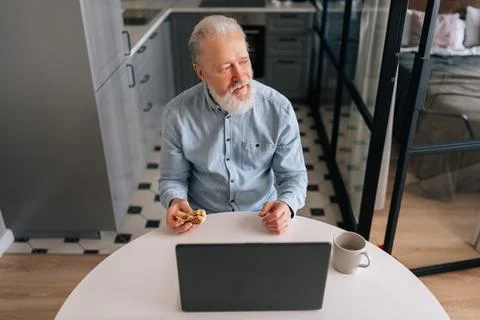 High-angle view of happy aged gray-haired man eating hamburger with beef from Stock Photos