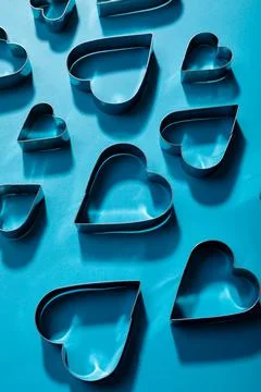 High angle view of heart shape pastry cutters with shadows on blue background Fotos de archivo