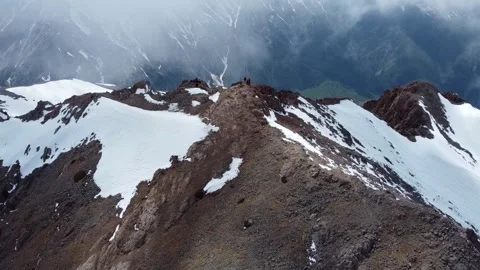 High angle view of hikers on narrow rocky mountain ridge with snow and clouds 库存影片 334326594