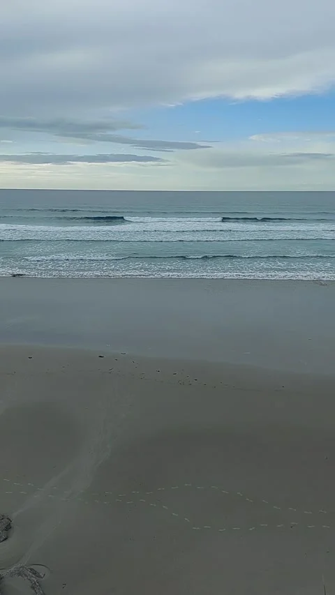 High angle view of human footprints on wet sand with ocean waves crashing on Stock-Footage 337323581