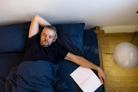 High-angle view of a man sleeping peacefully in bed. He s under a dark blue d Stock Photos