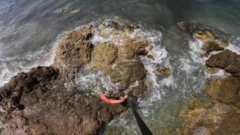 High angle view of man walking on sea rocks with camera pole Stock Footage 279864967
