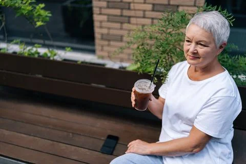High-angle view of mature aged woman drinking iced coffee, looking content and Stock Photos