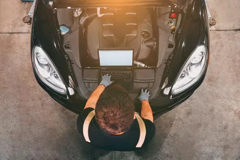 High angle view of mechanic examining car engine with help of laptop. Stock Photos