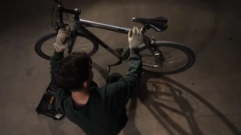 High angle view mechanic lying on the ground repairing a bicycle using hand Stock Footage 342768714
