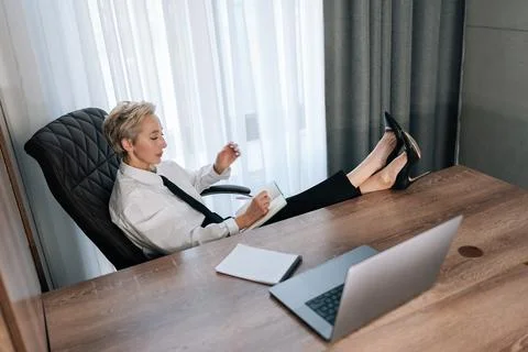High-angle view of middle-aged female CEO putting feet on desk with laptop Stock Photos