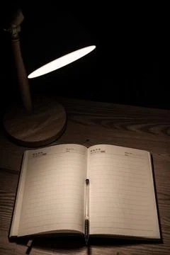 High angle view of an open blank diary on a wooden desk illuminated by a lamp. Foto stock