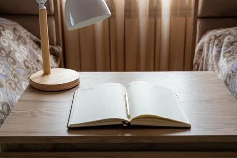 High angle view of an open notebook and desk lamp on a wooden surface. Stock Photos