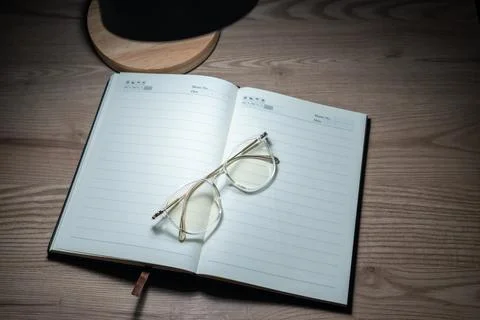High angle view of open notebook and glasses on wooden desk under spot light. Foto stock
