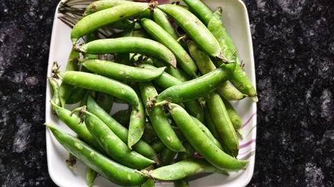 High angle view of organic garden peas in pods on dark granite background Видео 326021593