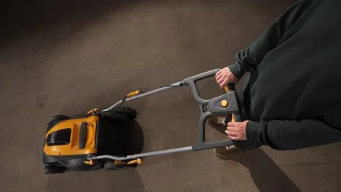 High angle view person holding the handle of an electric lawn mower, preparing Vidéo 342772690
