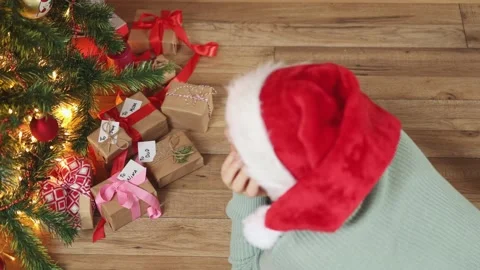 High angle view person red Santa hat wooden floor under Christmas tree gift box Stock Footage 165464691
