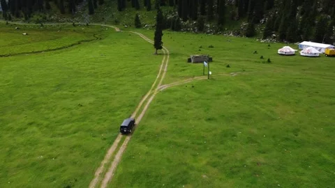 High angle view of off-road car driving on dirt road in green meadow with yurts Vidéo 334327051